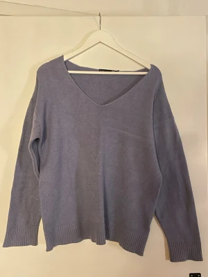 Ljuslila stickad tröja från 157 - Mysig ljuslila stickad tröja från 157 med v-ringning och avslappnad passform. Tröjan har ribbstickade muddar vid ärmslut och nederkant, perfekt för lager-på-lager. Tillverkad i mjukt material som känns skönt mot huden.