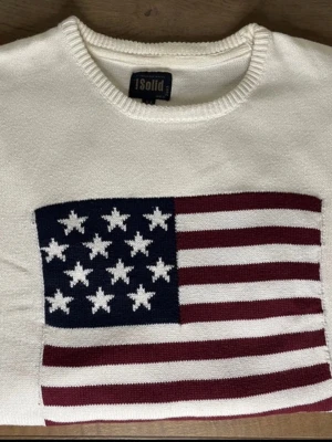 Vit tröja med USA flagga - strl M - !Solid - Vit stickad tröja av märket !Solid med en USA flagga som tryck i storkek M. Tröjan är i gott skick och har inga defekter utöver en liten fläck vid armhålan. 