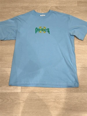 Blå Off-White t-shirt med tryck - Säljer en ljusblå t-shirt från Off-White med stort grafiskt tryck på ryggen och logga framtill. T-shirten har normal passform, korta ärmar och är gjord i mjuk bomull. Perfekt för dig som gillar streetwear och vill sticka ut med cool design. Aldrig använd! Skriv om ni är intresserade. Mvh 