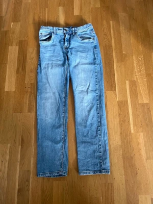 Ljusblå raka jeans - Säljer ett par ljusblå jeans med rak passform och klassisk femficksdesign. Jeansen har normal midja och subtila slitningar för en avslappnad look. Perfekta till vardagsstilen och passar till det mesta i garderoben.