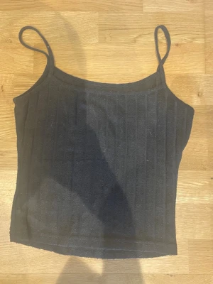 Svart linnetopp💕 - Snygg svart linnetopp med smala axelband och ribbad struktur. Toppen är croppad och har en enkel, stilren design. Perfekt för att ha nu på sommaren!🌻💕