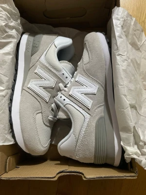 New Balance 574 grå sneakers 36,5 - StilrenaHELT NYA New Balance 574 sneakers i ljusgrå mocka och mesh med vita detaljer och den klassiska N-loggan på sidan. Skorna har en vit och grå sula samt grå hälkappa. Perfekta för dig som gillar en clean och sportig look. Storlek 36,5.