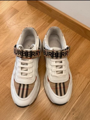 Burberry vita sneakers med logga - Säljer ett par vita Burberry sneakers med klassiskt rutmönster i beige, svart och rött. Storlek 44