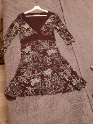 Chocolate brun blommig klänning/läng tunics med v-ringning från New Look - Snygg brun klänning/tunics med vit blommig print och v-ringad hals. Klänningen har trekvartsärm och markerad midja som ger en smickrande siluett. Perfekt för dig som gillar feminina detaljer och mönster. Mått på bilderna. 