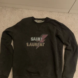 Saint Laurent sweatshirt  - SNABB AFFÄR mycket bra pris! Säljer en mörkgrå sweatshirt från Saint Laurent med tryckt logga och blixtdetalj på bröstet. Kom pm för fler bilder och detaljer.  