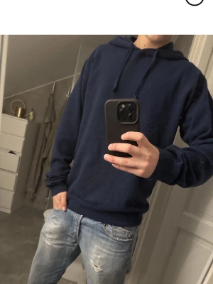 Mörkblå hoodie med dragsko - Säljer en mörkblå hoodie med klassisk huva och dragsko. Hoodien har ribbade muddar vid ärmslut och nederkant, samt en avslappnad passform. Perfekt för dig som gillar en enkel och stilren look.