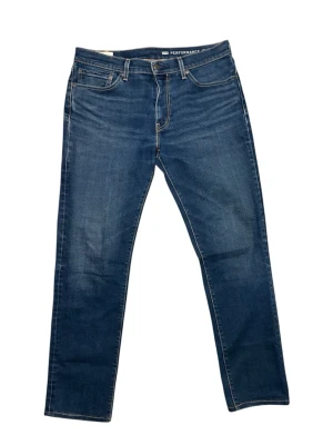 Blå Levi's jeans med rak passform - Klassiska blå jeans från Levi's med rak passform och fem fickor. Jeansen har kontrastsömmar, gylf med dragkedja och knapp samt Levi's ikoniska läderpatch bak i midjan. Tillverkade i stretchig denim för extra komfort. Storlek W33 L34