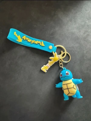 Blå Pokémon nyckelring Squirtle - Blå figur som föreställer Squirtle från Pokémon, med detaljer i gult och brunt. Tillverkad i plast och har en lekfull design. Perfekt som samlarsak eller dekoration för Pokémon-fans.