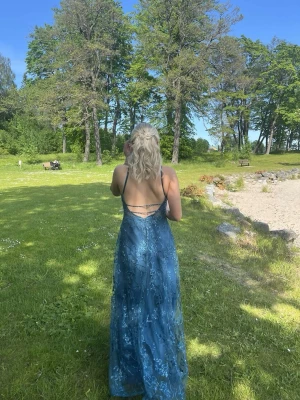 Balklänning - Supersnygg blå balklänning med tunna axelband och öppen rygg. Klänningen har vackra spetsdetaljer och paljetter. Jag är 160 cm lång och jag bär vanligtvis storlek S. Nypris 3233kr och den är endast använd en gång. 