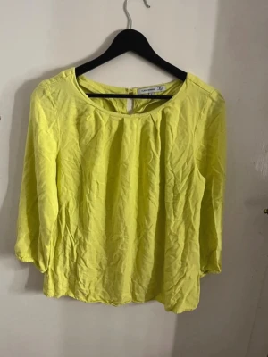 Gul blus från flash woman  - Fräsch gul blus från flash woman med rund halsringning och trekvartsärm. Blusen har ett litet nyckelhålsöppning bak och är tillverkad i ett lätt material som känns skönt mot huden. Perfekt för dig som gillar färg och enkel stil. Snygg gul topp/blus. Sitter fint på och är väldigt gullig. Om man stryker eller så så kommer den bli finare men den har legat i en låda ett tag. Fin passform och trekvartsärm. 