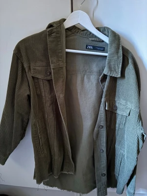 Olivgrön jeans jacka  från Zara - Olivgrön overshirt i bredspårig manchester från Zara. Modellen har klassisk krage, knappstängning och två bröstfickor med lock. Materialet är mjukt och ger en avslappnad look. Perfekt att bära som lager över t-shirt eller hoodie.