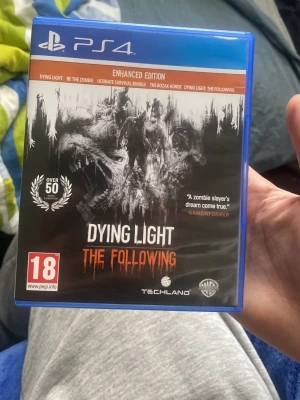 Dying Light: The Following PS4 - Dying Light: The Following Enhanced Edition till PS4. Ett actionfyllt zombiespel med öppen värld, mörka och intensiva miljöer och massor av överlevnadselement. Omslaget är svart med vita och orange detaljer och spelet är i ett blått plastfodral.