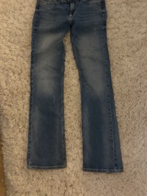 Blå bootcut jeans med slitningar - Snygga blå bootcut jeans med lätt slitna detaljer och klassisk femficksdesign. Jeansen har en något utsvängd passform nertill och är tillverkade i denim. Perfekta för en avslappnad och trendig look.