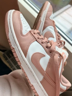 Nike Dunk Low rosa och vita sneakers - Nike Dunk Low sneakers i rosa o vit, använda ett fåtal gånger och normala i storlek . Pris går att diskuteras!