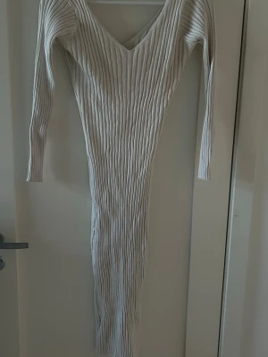 Klänning  - En figurnära ribbstickad klänning med långa ärmar. Klänningen når till mitten av vaden. Vit/cremefärgad storlek S. Lite nopprig 