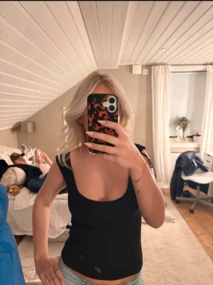 Svart croppad linnetopp - Snygg svart croppad linnetopp med breda axelband och djup urringning. Perfekt för att styla med jeans eller kjol för en trendig look.