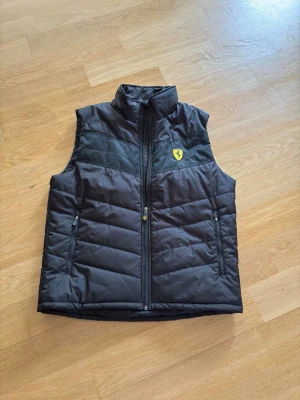 dunväst från Ferrari - Snygg svart dunväst från Ferrari. Perfekt för lager-på-lager och sportig stil. Väste är i mycket bra skick och utan några slitage eller märken.