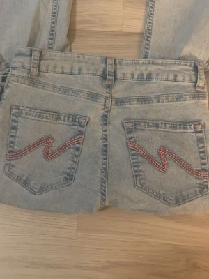 Nelly jeans  - Säljer mina ljusblå low waist jeans från Nelly med rosa detaljer och hål på knäna. Storlek 38 och använda endast 1 gång. Ordinariepris ca 700 