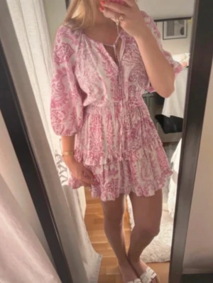  Ny trendig Rosa och vit kortklänning med volang - Supersöt kortklänning i rosa och vitt med blommigt mönster och volangdetaljer. Klänningen har v-ringning, trekvartsärm och resår i midjan för en smickrande passform. Perfekt för sommarens alla tillfällen!