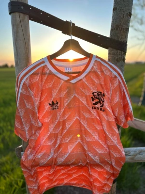 Holländsk retro fotbollströja Adidas - Orange retro fotbollströja från Adidas med klassiskt mönster, vita ränder på axlarna och svart KNVB-logga på bröstet. På ryggen står det CRUYFF och nummer 14. 