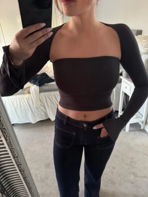 Grå offshoulder croppad topp - Trendig grå croppad topp med offshoulder-design och långa ärmar. Toppen är tight och har en stilren, minimalistisk look som passar perfekt till jeans eller kjol. Materialet känns mjukt och följsamt mot kroppen.