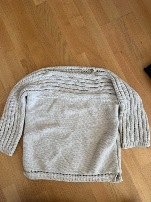 Beige stickad tröja med struktur - Säljer en beige stickad tröja med grovstickad struktur och horisontella ränder upptill. Tröjan har långa ärmar och en avslappnad passform. Perfekt för lager-på-lager och enkel att matcha med jeans eller kjol. Hittar inte storlek men det är en oversize tröja. Har fläckar som jag en testat att behandla, se bild. 