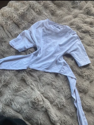 Vit topp med knytband - Trendig vit topp med knytband i midjan och korta ärmar. Perfekt för att skapa en cool och avslappnad look. Tillverkad i mjuk bomull som känns skön mot huden. Kanske små sminkfläckar på är ej säker men går bort i tvätten. 