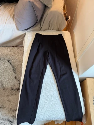 Svarta kostymbyxor med resårmidja - Snygga svarta kostymbyxor med rak passform och resår i midjan. Byxorna har en klassisk look med två fickor fram och är perfekta för en stilren outfit. Materialet är mjukt och följsamt, vilket ger en bekväm känsla hela dagen.