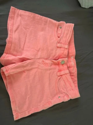 Rosa highwaist shorts från Cubus - Snygga rosa shorts från Cubus med hög midja och breda bälteshällor. Gjorda i mjuk bomull med klassisk knapp och dragkedja framtill. Perfekta för varma dagar och enkel att matcha med din favorit-topp.