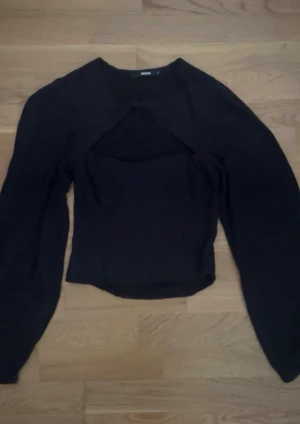 Svart långärmad topp med cut out från Bik Bok - Trendig svart långärmad topp från Bik Bok med snygg cut out-detalj framtill. Toppen har en figurnära passform och är tillverkad i mjukt material som känns skönt mot huden. Perfekt för dig som vill ha en stilren men ändå unik look. Aldrig använt den!