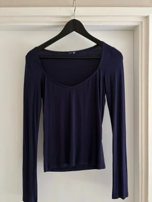 Mörkblå långärmad topp - En enkel och stilren mörkblå topp med lång ärm och v-ringad hals. Tillverkad i ett mjukt och stretchigt material som sitter skönt på kroppen. Perfekt att matcha med jeans eller kjol för en clean look.