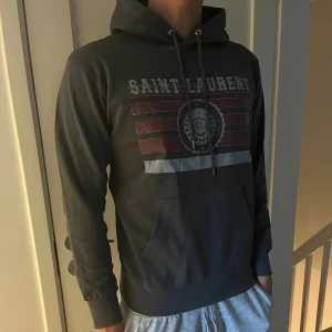 Grå Saint Laurent hoodie - Säljer nu min tvär feta hoodie ifrån Saknt Laurent. Det är storlek M men känns mer som en S. Den är köpt för 2500 för cirka ett halv år sedan där av kan jag ej garantera äntenhet då den är köpt här. Men väldigt bra skick och bara höra av sig vid funderingar!!