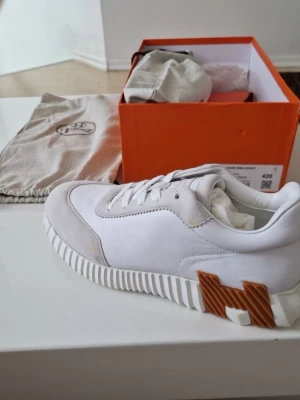 H skor - Snygga vita sneakers från H med unika räfflade sulor och en stor brun H-detalj på sidan. Skorna är låga och har ovandel i läder och mocka. Perfekta för dig som vill sticka ut med exklusiva och trendiga sneakers.