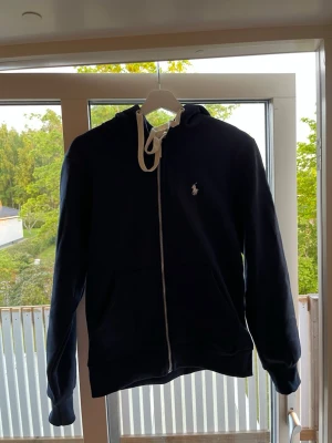 Mörkblå hoodie från Polo Ralph Lauren - Snygg mörkblå hoodie med dragkedja från Polo Ralph Lauren. Det är storlek M men passar över S.  Hör av er vid frågor!