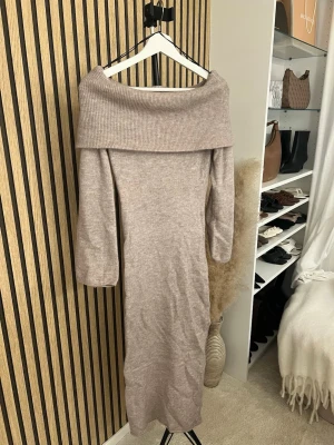 Beige stickad offshoulder klänning - Mysig beige stickad långklänning med bred offshoulder-krage och långa ärmar. Perfekt för dig som gillar en avslappnad men ändå stilren look. Materialet är mjukt och stretchigt, vilket gör den extra bekväm. Skriv om ni vill ha bild på 🫶🏼🫶🏼