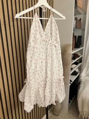 Vit blommig sommarklänning med volang - Söt vit kortklänning med små rosa blommor, tunna axelband och volang nertill. Klänningen har omlottkänsla upptill och är perfekt för varma dagar. Tillverkad i lätt bomullstyg som känns luftigt och bekvämt. Insydd i sidan men går att sprätta upp lätt om man skulle vilja!  Skriv om ni vill ha bild på 🫶🏼🫶🏼