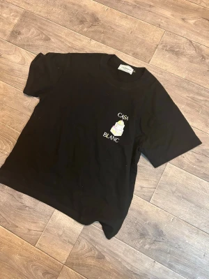 Svart Casa Blanca t-shirt med tryck - Svart t-shirt från Casa Blanca med färgglatt tryck och text på både bröstet och ryggen. T-shirten har klassisk passform och är tillverkad i mjuk bomull. Perfekt för dig som gillar streetwear och snygga prints.