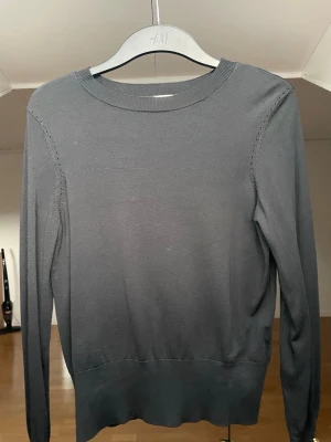 Snygg tröja - En enkel och stilren svart tröja från H&M. Tröjan har rund halsringning, långa ärmar och guldiga knappar vid ärmslut. 