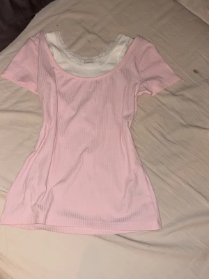 Lite elena Gilbert vibe med en tröja med insyd spets linne under - Supersöt ljusrosa ribbad topp med korta ärmar och rund halsringning. Under finns en vit insydd topp med spetskant som ger en 2000s vibe . Perfekt för dig som gillar en feminin och trendig stil. Köpes via Swish eller direkt i appen men skriv helst innan då jag även säljer den på Vinted!