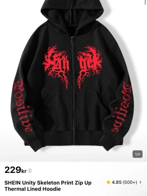 Svart hoodie med röd tryck från SHEIN - Svart hoodie med dragkedja från SHEIN, fodrad för extra värme. Har rött tryck med texten 'Positive' på ärmarna och ett coolt grafiskt tryck på bröstet. Utrustad med huva och fickor framtill. Perfekt för en edgy streetstyle.