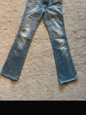 Ljusblå lowwaist bootcut jeans - Säljer ett par ljusblå bootcut jeans med klassisk femficksdesign och snygga slitningar framtill. Jeansen har låg midja och är tillverkade i denim med lite stretch för extra komfort. Perfekta för en avslappnad och trendig look.