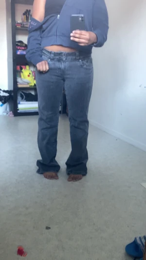 Grå bootcut jeans med låg midja - Säljer ett par gråa bootcut jeans med låg midja och klassisk femficksdesign. Jeansen har en lätt tvättad look och vida ben nedtill för en avslappnad och trendig stil. Perfekta för dig som gillar en retro vibe och vill ha ett par jeans som sticker ut. På baksidan av jeansen så har baksidan rivits lite som visas i bilderna 