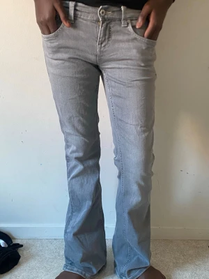 Grå bootcut jeans med broderade fickor - Snygga grå bootcut jeans med broderade detaljer på bakfickorna. Jeansen har klassisk femficksdesign, normalhög midja och stängs med knapp och dragkedja. Perfekta för dig som gillar en avslappnad men trendig stil. De är långa på mig som är 153.