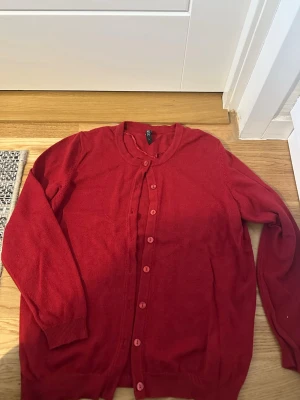 Röd kofta välanvänd stl L  - Röd kofta  med rund halsringning och knappar framtill. Långärmad modell i mjukt, tunt stickat material. Perfekt att slänga över en t-shirt eller linne för extra lager. Välanvänd dock hel 