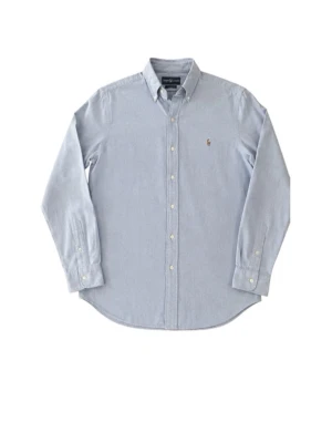 Blå skjorta från Ralph Lauren - Klassisk ljusblå skjorta från Ralph Lauren med button-down krage och broderad logga på bröstet. Skjortan är långärmad, har knappar framtill och är tillverkad i bomull. Perfekt för en clean och stilren look.