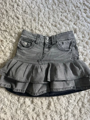Grå volangkjol i denim - Säljer en grå jeanskjol med volangkant och klassiska fickor fram och bak. Kjolen har bälteshällor, knapp och dragkedja framtill samt en snygg volangdetalj nedtill som ger en cool och trendig look. Sytt om ett par grå jeans från gina till en vacker stil ren volangkjol! Ej fast pris💞💞