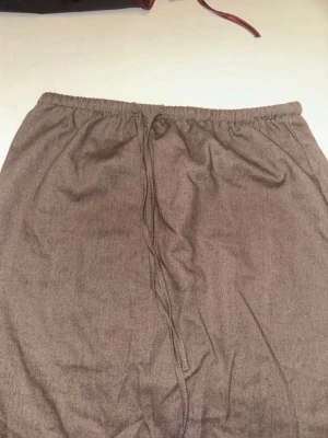 Brun långkjol med snörning - En enkel och stilren brun långkjol i linne material  med snörning i midjan. Kjolen har rak passform och är i linne tror jag. Materialet  känns bekvämt mot huden. Perfekt för dig som gillar en avslappnad look med ett skönt material.☺️ Finns tyvärr ingen lapp med storlek på kjolen men skulle gissa på S/M sen går det att justera med hjälp av de justerbara banden i midjan ❤️