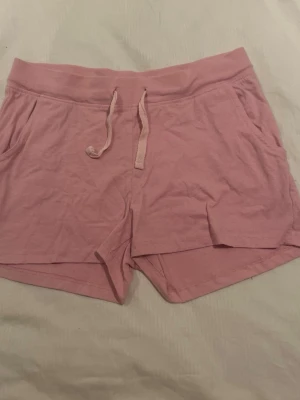 Rosa mjuka shorts med snörning - Säljer ett par ljusrosa shorts med snörning i midjan och fickor på sidorna. De är tillverkade i mjuk bomull och har en avslappnad passform, perfekta för varma sommardagar eller chill hemma.