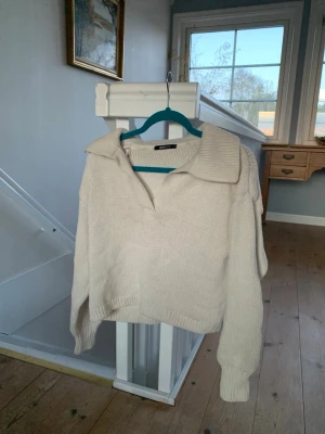 Beige stickad tröja med krage - Snygg beige stickad tröja från NA-KD med stor krage och v-ringning. Tröjan har lång ärm och ribbade muddar vid ärmslut och nederkant. Perfekt för lager-på-lager och en avslappnad stil.