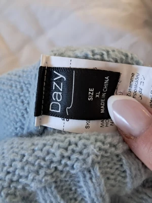 Ljusblå stickad tröja från Dazy - Ljusblå stickad tröja från Dazy med rund halsringning och ribbade muddar vid ärmslut och nederkant. Tröjan har en avslappnad passform och är perfekt för lager på lager. Enkel och stilren design som passar till det mesta.